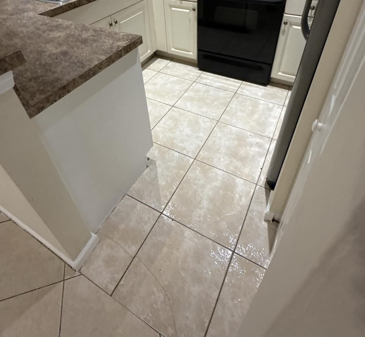 Cleaned galley kitchen with white cabinets, a stone-look counter and a beige tile floor washed to a shine